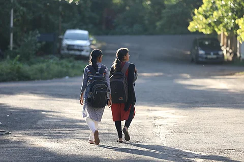 Two girls walking on the road with their school bags with their backs to the camera
