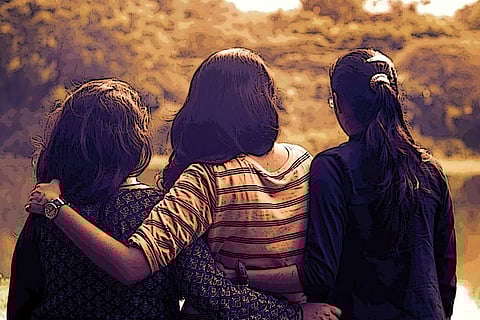 Image of three young women hugging each other and looking into the sun set
