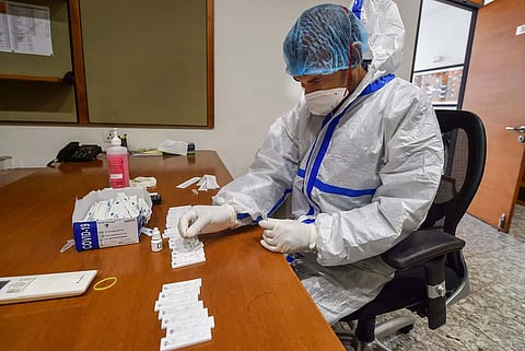 Health worker wearing mask and gloves sitting at a table conducting COVID-19 test