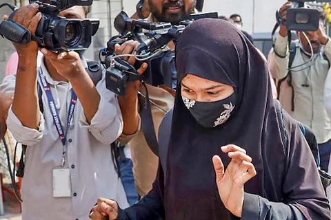 A hijab-clad student turning away from cameras as she walks towards her exam hall