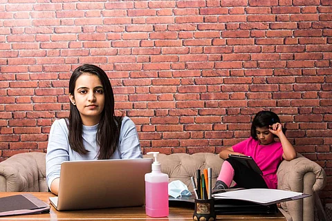 A representative image of a mother working from home, while her child studies in the background.