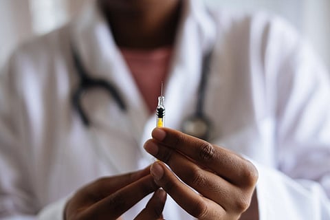 A doctor in white coat and a stethoscope around neck holding up a syringe
