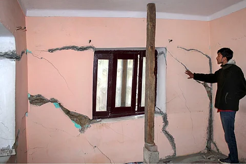 A person standing next to large cracks on the wall of a house