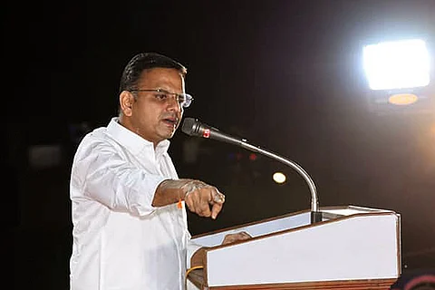 KT Raghavan stands on a podium and points with his right hand