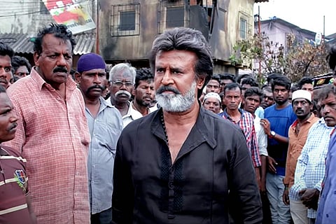 Rajinikanth in a black shirt standing with a crowd behind him in Kaala