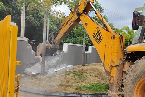Excavator demolishing a compound wall