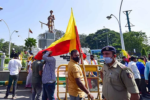 Man holding a Karnataka Flag in front of a statue of Sangolli Rayanna