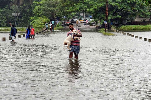 A man carrying his pet dog wades through the flooded Vellayani Kakkamoola road during heavy rain in Thiruvananthapuram on October 16 2021