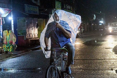 A man covers himself with a plastic sheet during rains in Thiruvananthapuram