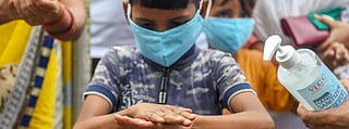 A small boy in mask sanitising his hands