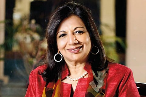 Kiran Mazumdar Shaw in a red outfit, facing the camera and smiling looking slightly to her left