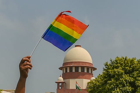 A person's hand waving a rainbow flag against the backdrop of Supreme Court