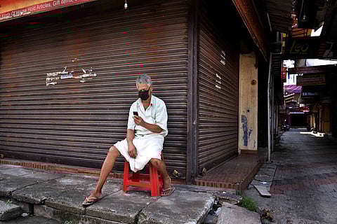 A man wearing mask, sitting in front of shop the shutters of which are down, during a lockdown day in Kerala