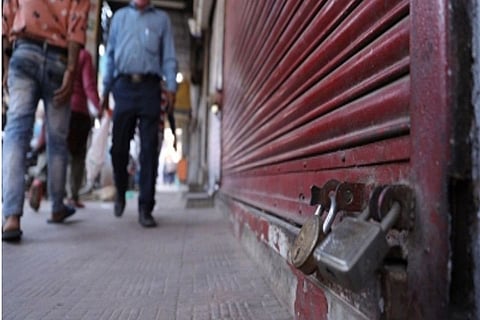 Two men walking past a closed shutter of a shop with a lock on it