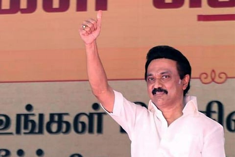 DMK leader MK Stalin in a white shirt with his right hand raised to show victory