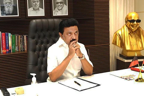 MK Stalin sits before a desk with his hands on his chin, as a bust of Karunanidhi sits in the right hand corner