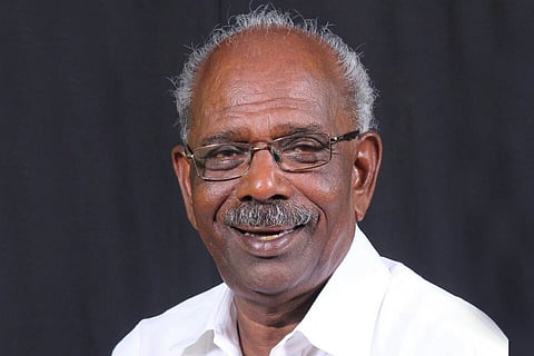 Kerala MLA MM Mani in a white shirt and spectacles, smiling and facing towards the camera, against a black backdrop