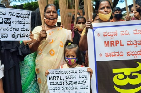 Women and a child wearing face masks hold placards and brooms during a protest against pollution from the MRPL refinery in Mangaluru.