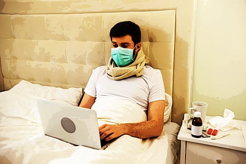 Man Working In Bed Wearing Medical Mask. Man Working At Home. Man Using Laptop In Bed