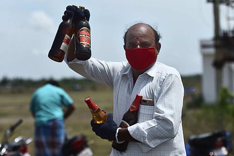 A masked man holding up bottles of liquor purchased during the coronavirus pandemic