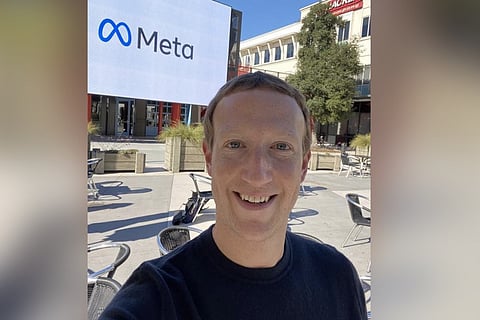 Mark Zuckerberg takes a selfie in front of a while hoarding with Meta written on it