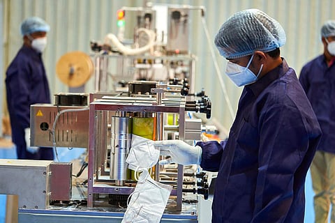 A worker examines a mask at a manufacturing plant as two others stand in the background