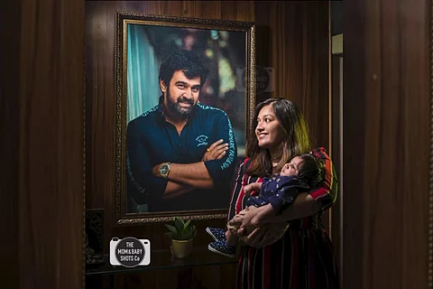 Meghana Raj Sarja holding her baby in front of a portrait of Chirranjeevi Sarja