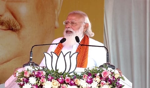 PM Modi picture with lotus symbol speaking at a meeting, facing mike in Puducherry
