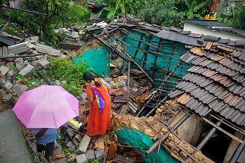 Locals walk past a partially collapsed house due to heavy monsoon rain in Chikmagalur