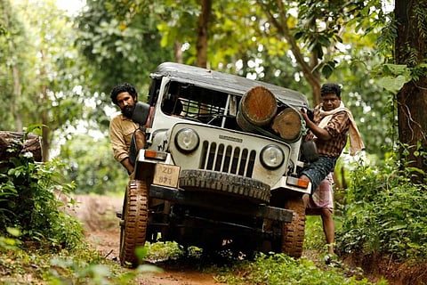 Two men in a jeep carrying logs driving through a green forest
