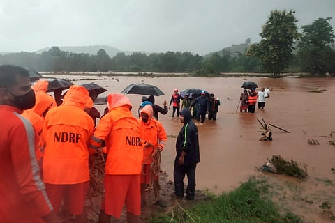 NDRF officials in fluorescent orange jackets standing next to a flooded river