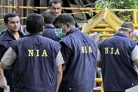 Persons wearing navy-blue colored sleeveless coats with the letters NIA on them