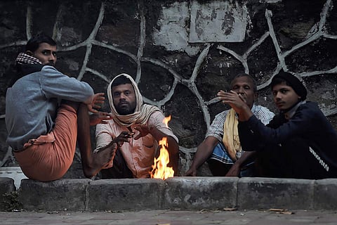 People gather around a fire for warmth amid the cold temperature in New Delhi