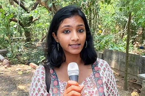 Newslaundry journalist Nidhi Suresh holds a microphone against a background a trees
