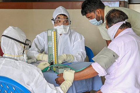 Healthcare workers in full protective gear check the blood pressure of a man during a medical screening. Image used for representation
