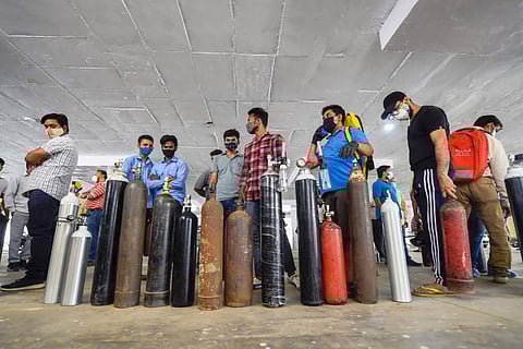 A group of people, each standing with holding an oxygen cylinder outside a hospital
