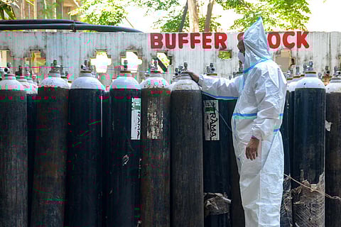 A health worker standing in front of a line of oxygen cylinders arranged outside a hospital