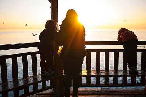 A woman with two children outdoors during sunset