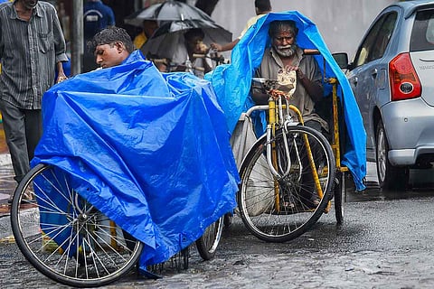 Two persons with disability riding in a wheelchair covering themselves under a blue sheet in rain