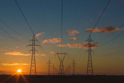 Powerlines located against the backdrop of sun setting in the left corner of a blue sky