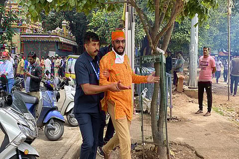 A man in saffron shirt wearing a saffron headband is being taken away by a policeman in safari suit during protest at Eidgah maidan in Bengaluru