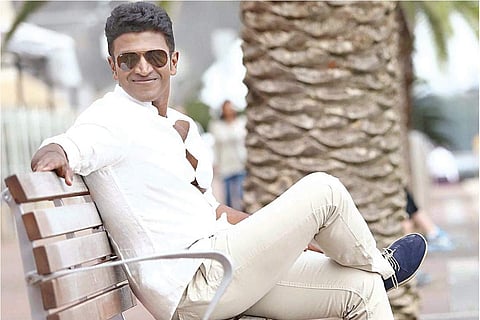 Puneeth Rajkumar sitting on a bench in a white shirt and white pants