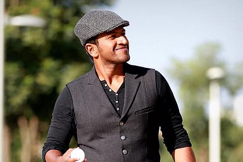 Puneeth Rajkumar in a dark vest and golfer's cap looking to the left