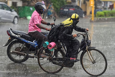 A cyclist and a two-wheeler rider riding in heavy rain
