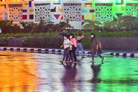 People holding an umbrella cross a road during heavy rain in Bengaluru