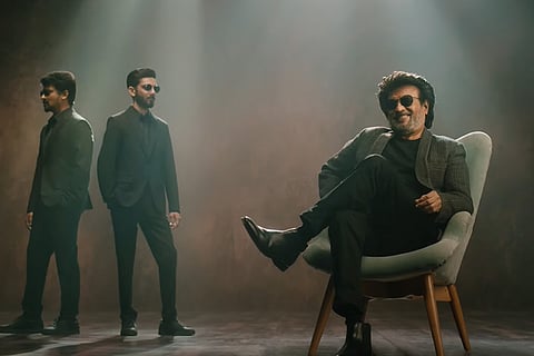 Actor Rajinikanth is seated in a chair, while director Nelson and composer are standing behind him.