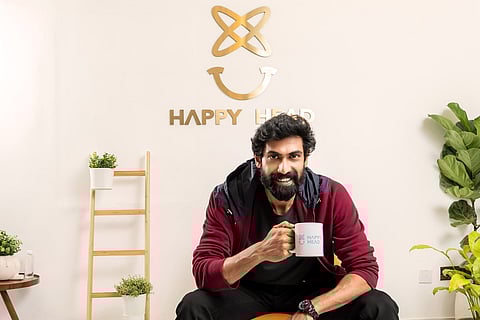 Rana Daggubati in maroon and black sitting with a coffee mug