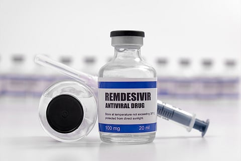 A standing vial of remdesivir with a syringe behind it and another vial next to it