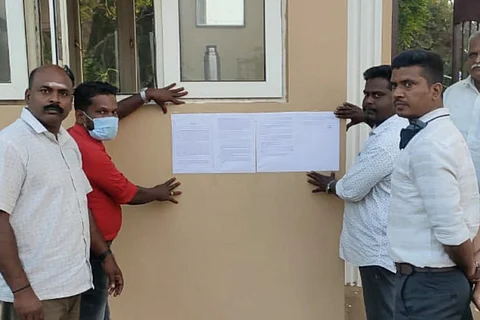 Four district officials sticking an eviction notice on the gate of the university
