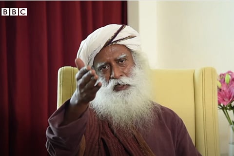Jaggi Vasudev in a brown colored attire, white color turban, pointing his hands towards the screen, with an angry expression in his face